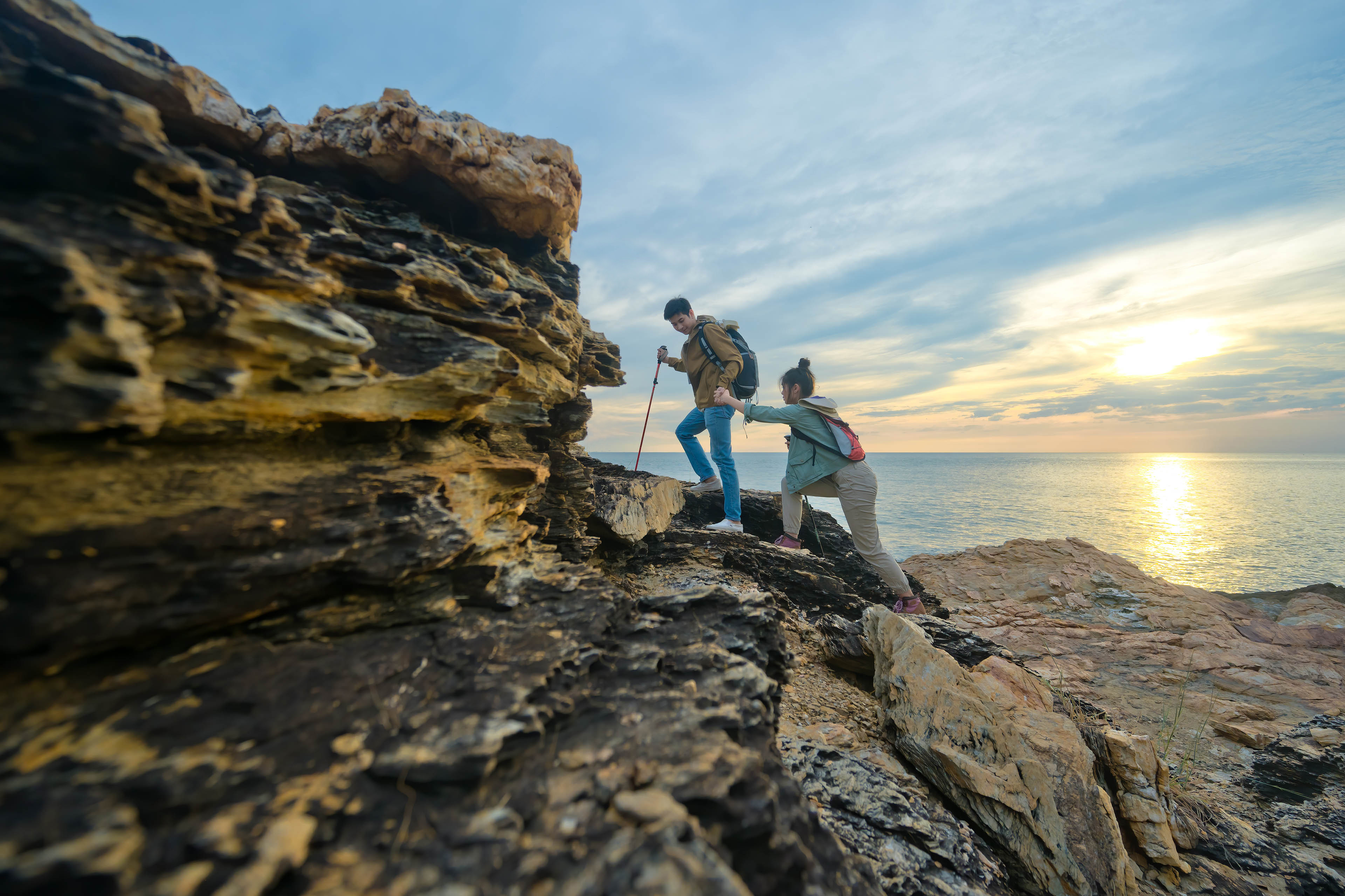 Hiker Woman helping her friend reach the top of the mountain